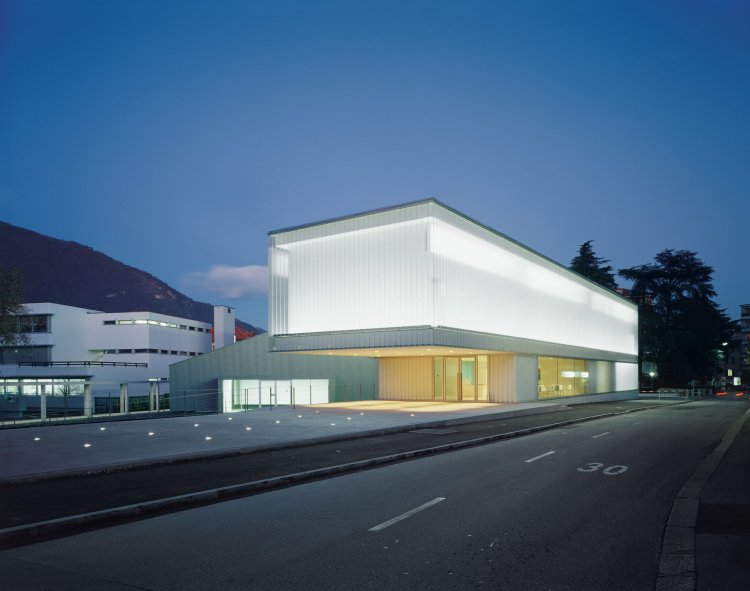 Nachtaufnahme eines modernen Museumsbaus, dessen Fassade vollständig aus transluzenten U-Glaselementen besteht. Das Gebäude leuchtet von innen heraus gleichmässig warm und hebt sich als heller Quader aus der dunklen Umgebung ab.