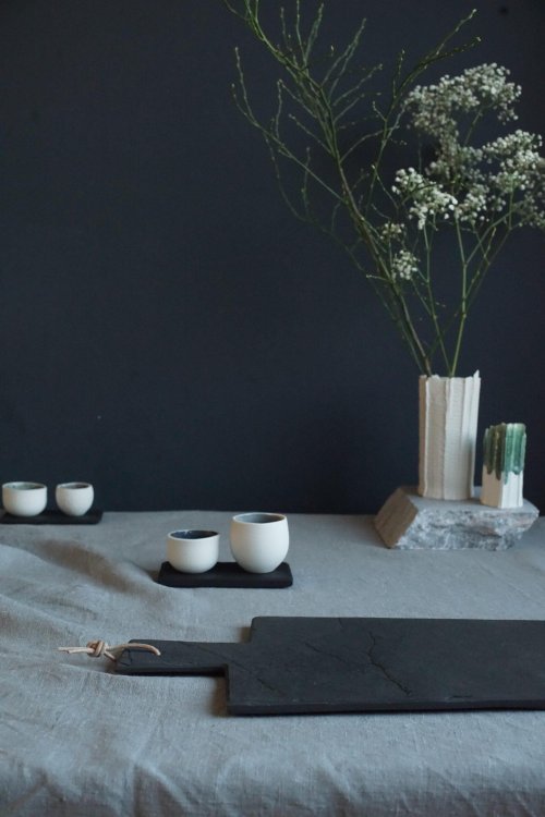 Zu sehen ist ein Tisch mit einem Schieferbrett, eine Vase mit Blumen und mehrere kleine Steinzeug-Schalen.